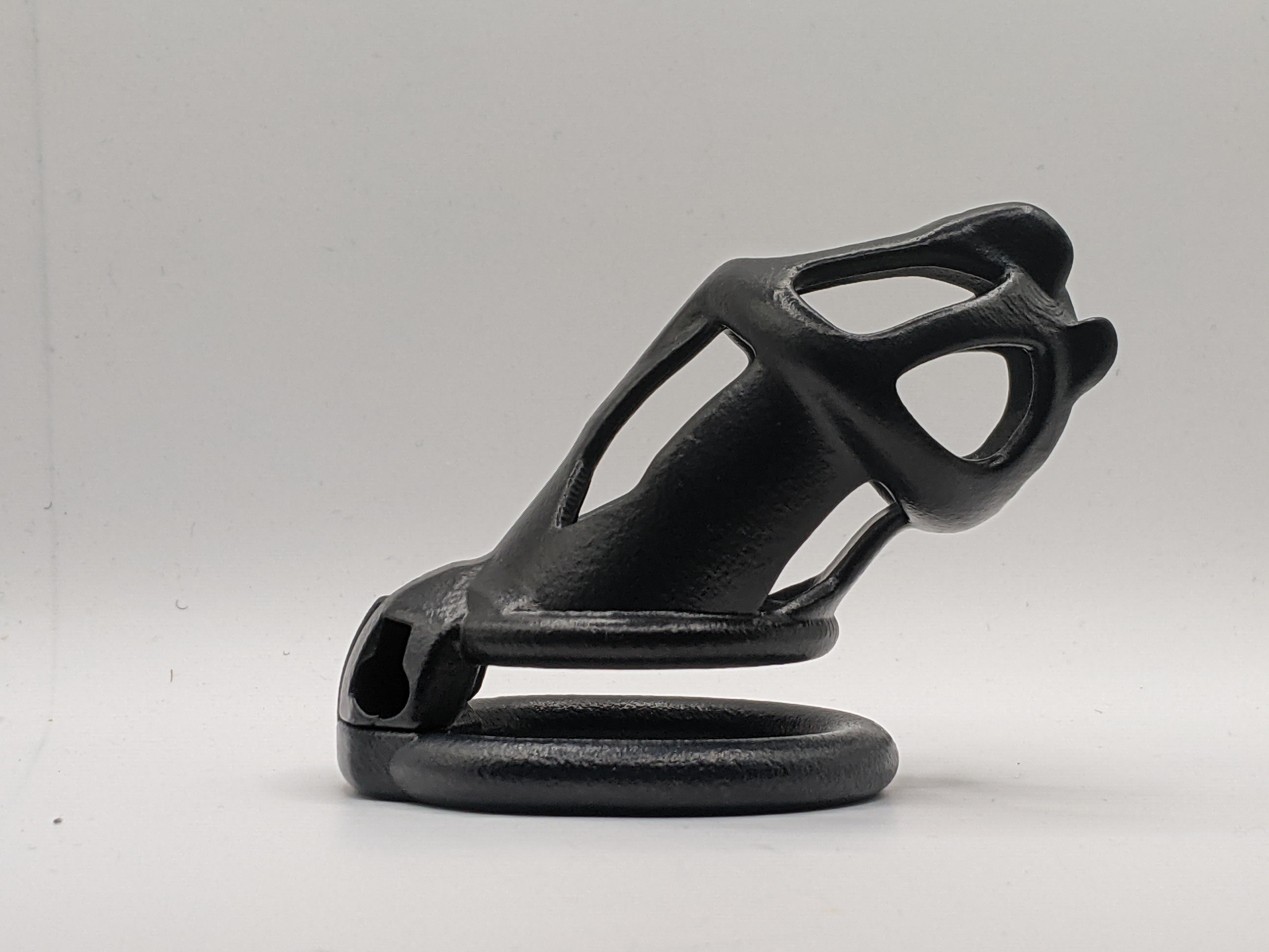 A black chastity cage with a metallic lock and two keys, designed to accommodate foreskins or circumcised individuals.